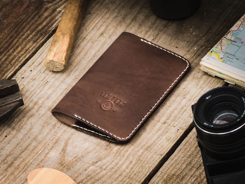 May include: A brown leather passport holder with white stitching and the word "Voyage" embossed on the front.