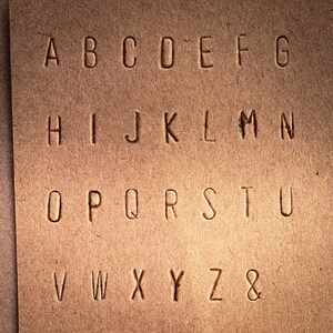 May include: A close-up of a brown paper surface with the alphabet A through Z and the ampersand symbol printed in a simple, sans-serif font.