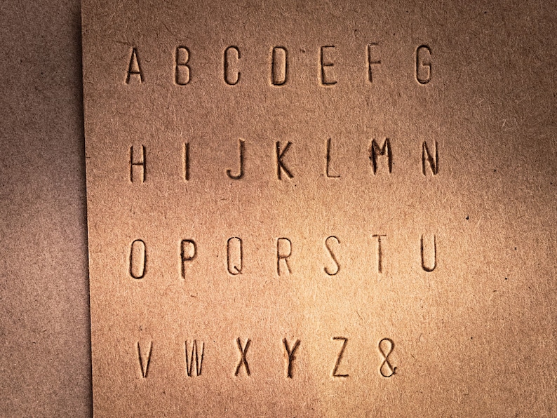 May include: A close-up of a brown paper surface with the alphabet A through Z and the ampersand symbol printed in a simple, sans-serif font.
