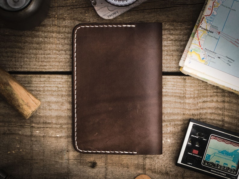 May include: A brown leather wallet with white stitching. The wallet is lying on a wooden surface.