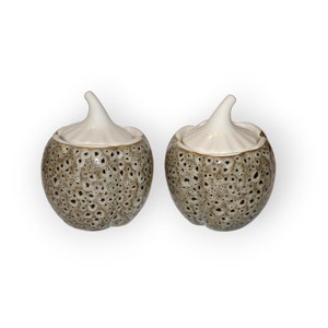 Puede incluir: Dos recipientes de cerámica con forma de ajo con tapas. Los recipientes son marrones con un patrón moteado y las tapas son blancas.