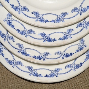 May include: A stack of five white ceramic plates with a blue floral pattern around the edge.
