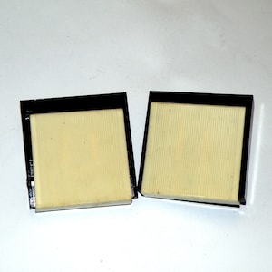 May include: Two black framed square filters with a white, textured surface.