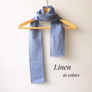 May include: A light blue linen scarf hanging on a wooden hanger. The scarf has a frayed edge. Linen. 16 colors.