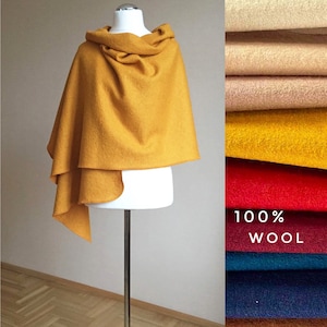 Peut inclure: Cape en laine jaune moutarde drapée sur un mannequin, avec un col roulé et un design superposé. Un nuancier de tissus de laine de différentes couleurs, dont rouge, sarcelle et marine, est affiché à côté de la cape. Le texte "100% WOOL" est visible.