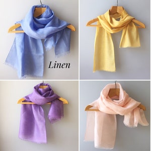 May include: Four linen scarves displayed on hangers. The scarves are in blue, yellow, purple, and pink.