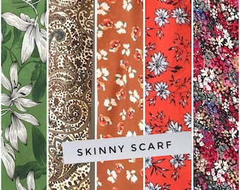 Könnte beinhalten: Vier verschiedene Stoffmuster mit Blumenmustern. Die Muster sind vertikal angeordnet und mit "SKINNY SCARF" beschriftet. Die Stoffe sind grün mit weißen Blumen, braun mit goldenem Paisley, orange mit weißen Blumen und rot mit weißen Blumen.