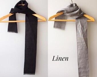 Könnte beinhalten: Zwei Leinenschals hängen an Holzbügeln. Der Schal links ist schwarz und der Schal rechts ist hellgrau. Der Text "Linen" ist in Schwarz auf weißem Hintergrund geschrieben.