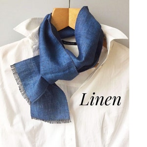 May include: A blue linen scarf with frayed edges, displayed on a white shirt. The word "Linen" is written in black text on the shirt.