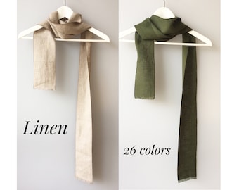 Könnte beinhalten: Zwei Leinenschals hängen an weißen Kleiderbügeln. Der Schal links ist hellbeige. Der Schal rechts ist dunkelgrün. Der Text "Linen" befindet sich unter dem beigen Schal und der Text "26 Farben" unter dem grünen Schal.