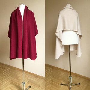 Pode incluir: Duas echarpes de caxemira, uma em vermelho bordô escuro e a outra em bege claro, expostas em manequins. Ambas as echarpes estão drapeadas sobre os ombros dos manequins, mostrando sua textura macia e seu caimento fluido.