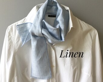 Könnte beinhalten: Ein hellblauer Leinenschal mit ausgefransten Kanten, gebunden um den Kragen eines weißen Hemdes mit Knöpfen. Das Wort "Leinen" ist in schwarzer Kursivschrift auf dem Hemd geschrieben.