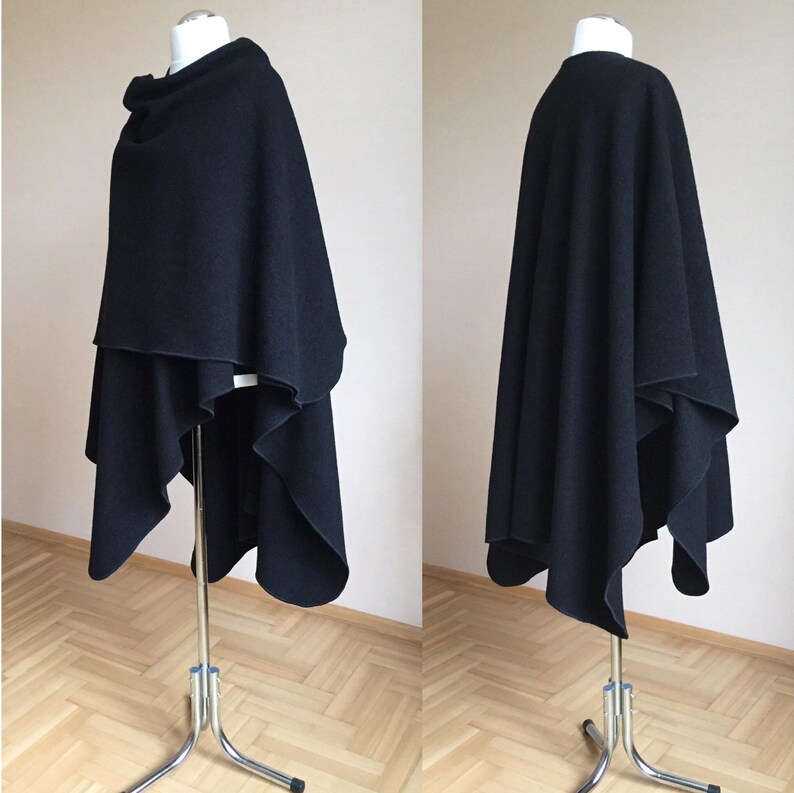 May include: A black wool wrap with a draped design. The wrap is shown on a mannequin and is folded in a way that creates a long, flowing shape.