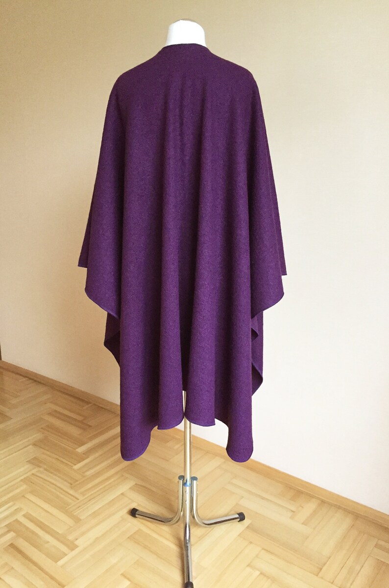 May include: A purple wool poncho draped over a mannequin. The poncho is a simple design with no embellishments.
