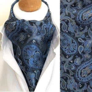 Könnte beinhalten: Ein marineblauer Ascot mit einem detaillierten Paisley-Muster in Blau- und Grautönen. Der Ascot wird über einem weißen Hemd mit Kragen getragen und zeigt das komplizierte Design und die Textur des Stoffes.