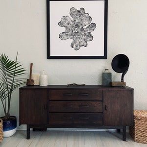 May include: A dark wood dresser with three drawers and a cabinet door. The dresser has black hardware and sits on a white wood floor. A black and white print of a tree trunk cross-section hangs on the wall above the dresser.