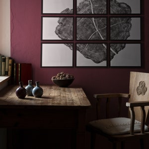 May include: A wooden table with a dark brown finish sits in a room with a burgundy wall. A chair with a carved wooden back and a white cushion sits next to the table. Three small ceramic vases sit on the table, and a bowl of dried berries sits on the table in front of the chair.