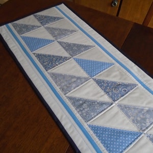 May include: A white table runner with a blue and white geometric pattern. The runner has a navy blue border with a light blue stripe.