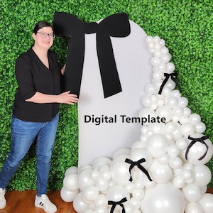 May include: A white arch-shaped backdrop with a large black bow and a cascade of white balloons, accented with black bows. The words "Digital Template" are printed on the backdrop. A woman is standing next to the backdrop.