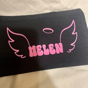 May include: Black canvas zippered pouch with pink angel wings and a halo above the name "HELEN" in pink retro-style lettering.