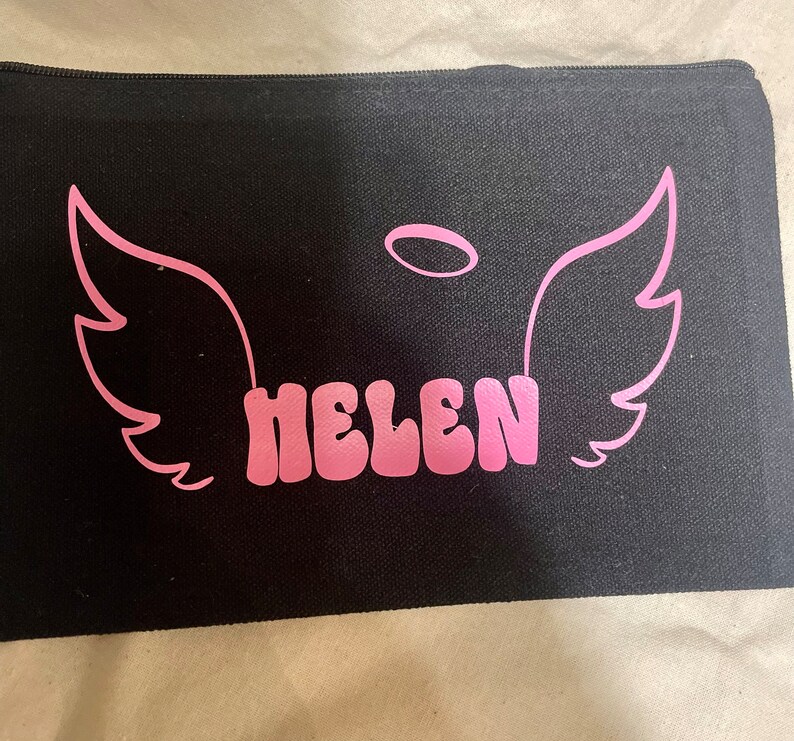 May include: Black canvas zippered pouch with pink angel wings and a halo above the name "HELEN" in pink bubble letters.