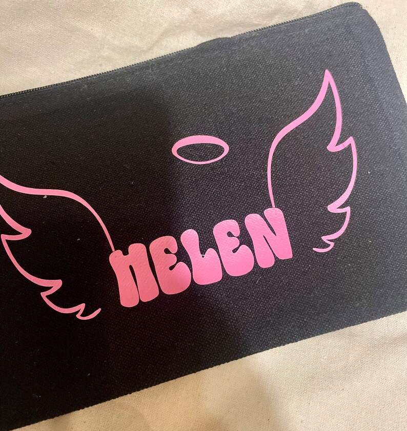 May include: Black canvas zippered pouch with pink angel wings and a halo, and the name "HELEN" in pink letters.