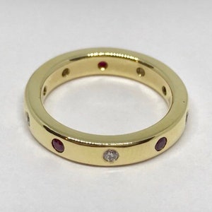 May include: A gold band ring with a single diamond and multiple ruby stones set in the band.