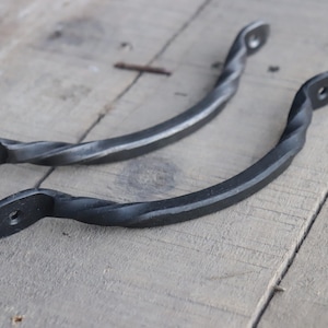 May include: Two black metal twisted drawer pulls. The pulls are about 5 inches long and have a simple, rustic design.