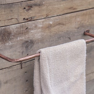 May include: A copper towel bar mounted on a wooden wall with a towel hanging on it.