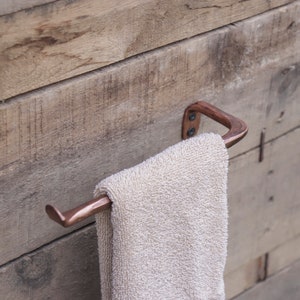 May include: A copper towel rack mounted on a wooden wall with a white towel hanging on it.