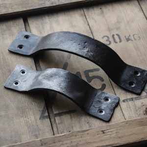 May include: Two black metal door handles with a curved design and two holes on each side. The handles are on a wooden surface with the text "30 KG" printed on it.