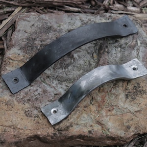 May include: Two black metal door handles with a curved design. The handles are on a rock surface.