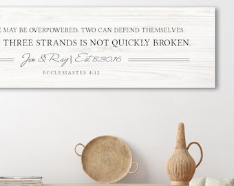 May include: A white wood sign with a black text quote: "Though one may be overpowered, two can defend themselves. A cord of three strands is not quickly broken." The quote is attributed to "Jou & Ray Eit 8.3016" and "Ecclesiastes 4:12".