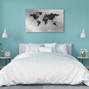 May include: A white bed with white bedding and pillows in a bedroom with a world map print on the wall. The map is black and white with red pins marking locations. The text on the map reads "Jason & Megan, Our world is small, our adventure means so much, May 2019."