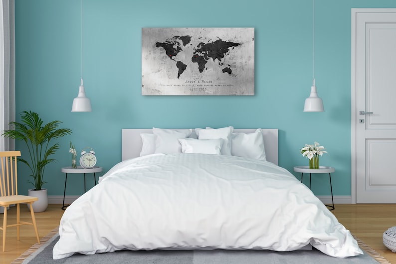 May include: A white bed with white bedding and pillows in a bedroom with a world map print on the wall. The map is black and white with red pins marking locations. The text on the map reads "Jason & Megan, Our world is small, our adventure means so much, May 2019."