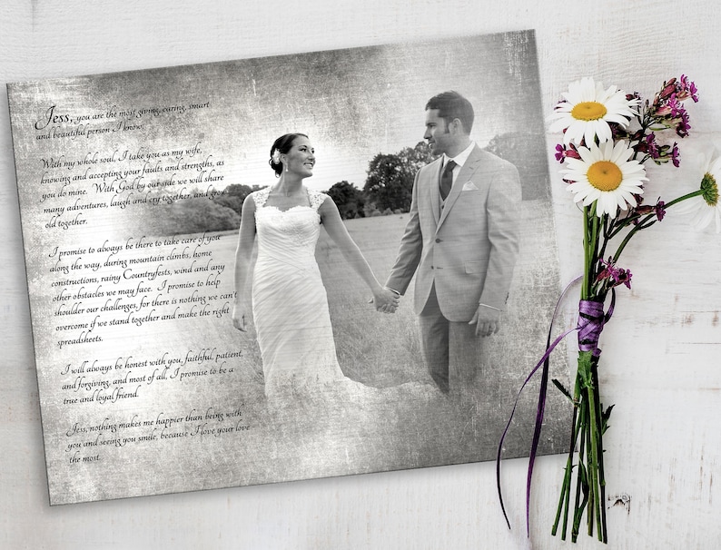 May include: A rectangular print featuring a black and white photograph of a couple holding hands in a field, overlaid with black cursive text of wedding vows. The print is displayed next to a bouquet of white daisies and purple flowers.