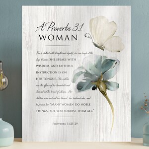 May include: A white wood background with a blue and green watercolour flower and butterfly. The text "A Proverbs 31 Woman" is at the top of the image. The text continues with a quote from Proverbs 31:25-29, "She is clothed with strength and dignity...Many women do noble things, but you surpass them all."