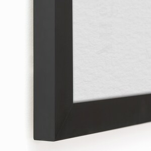 以下が含まれることがあります： 白いマットが付いた黒い額縁のクローズアップ。額縁は木でできており、シンプルでモダンなデザインです。
