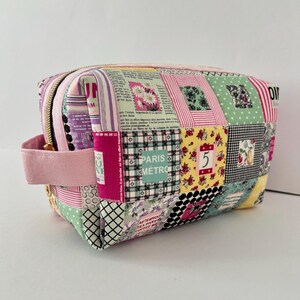 Puede incluir: Un neceser de patchwork con una variedad de patrones de tela, incluyendo estampados florales, a rayas y de periódico. La bolsa tiene un asa rosa y una cremallera dorada. El texto "PARIS METRO" es visible.