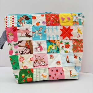 May include: A quilted zipper pouch featuring a patchwork design of various colorful fabric squares. The patterns include illustrations of children, animals, mushrooms, strawberries, bicycles, and geometric shapes in shades of red, blue, yellow, and green.