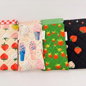 May include: Four rectangular quilted fabric pouches with a metal frame closure. The first is cream with red strawberries and a red gingham trim. The second is cream with ice cream cones. The third is green with strawberries and a green gingham trim. The fourth is black with red strawberries.