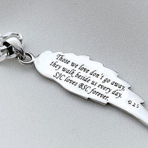 May include: Silver pendant necklace with a feather charm. The feather has an inscription that reads: "Those we love don't go away, they walk beside us every day. SIC loves BSC forever." The pendant is attached to a silver curb chain.