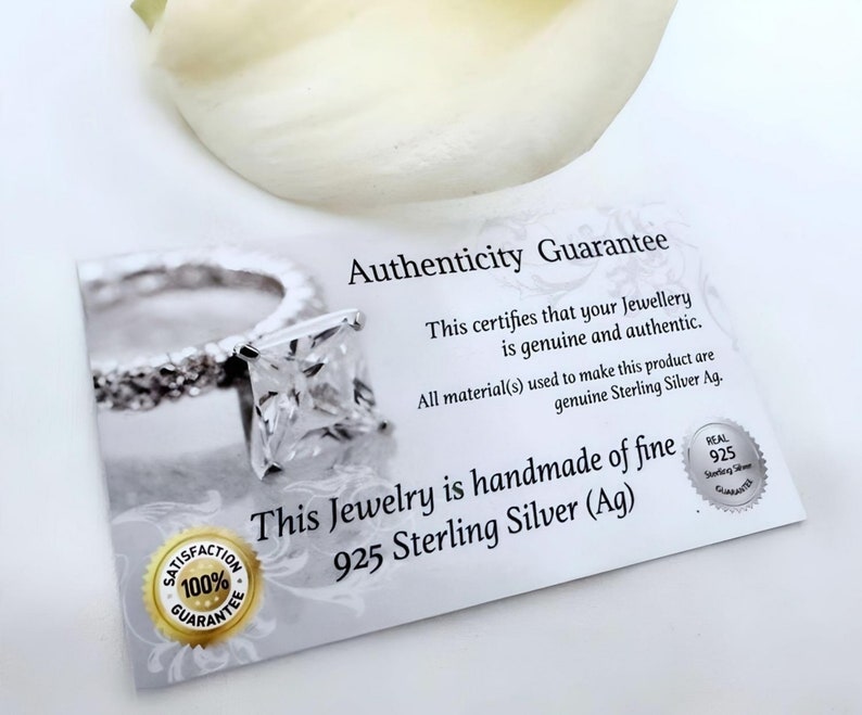 以下が含まれることがあります： 「Authenticity Guarantee」と「This certifies that your Jewellery is genuine and authentic. All material(s) used to make this product are genuine Sterling Silver Ag. This Jewelry is handmade of fine 925 Sterling Silver (Ag)」と書かれた白いカード。カードには、正方形の石がついた銀の指輪が描かれている。カードには、100%満足保証シールと本物の925スターリングシルバー保証シールも貼られている。