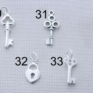 May include: Four silver-toned metal charms labeled with numbers 30, 31, 32, and 33. Charm 30 is a skeleton key, 31 is a decorative key with a circular top, 32 is a heart-shaped padlock, and 33 is a key with an ornate, openwork circular head.