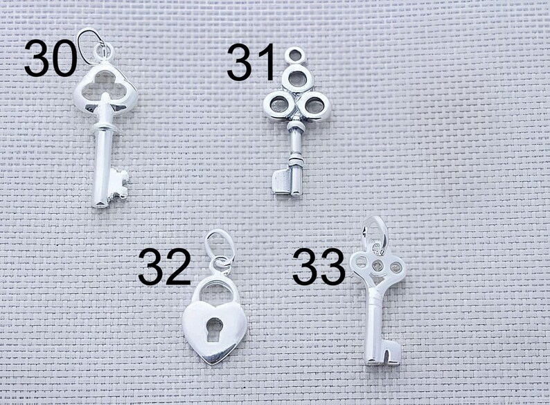 May include: Four silver-toned metal charms labeled with numbers 30, 31, 32, and 33. Charm 30 is a skeleton key, 31 is a decorative key with a circular top, 32 is a heart-shaped padlock, and 33 is a key with an ornate, openwork circular head.