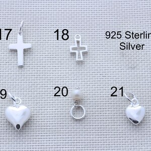 May include: A collection of 925 sterling silver jewelry charms labeled 17 through 21. The set includes a solid cross, an open-frame cross, two smooth heart charms, and a small circular charm featuring a single white pearl bead.