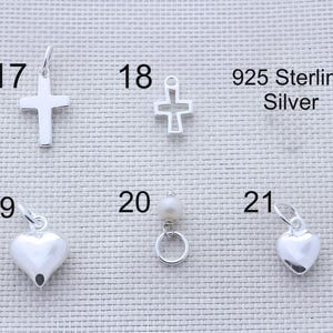 Puede incluir: Una colecci&oacute;n de dijes de plata esterlina 925 numerados del 17 al 21. El art&iacute;culo 17 es una cruz s&oacute;lida, 18 una cruz de marco abierto, 19 un coraz&oacute;n liso, 20 una perla peque&ntilde;a en un anillo de plata y 21 un dije de coraz&oacute;n liso m&aacute;s peque&ntilde;o.