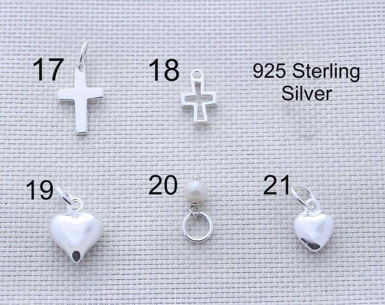 Puede incluir: Una colecci&oacute;n de dijes de plata esterlina 925 numerados del 17 al 21. El art&iacute;culo 17 es una cruz s&oacute;lida, 18 una cruz de marco abierto, 19 un coraz&oacute;n liso, 20 una perla peque&ntilde;a en un anillo de plata y 21 un dije de coraz&oacute;n liso m&aacute;s peque&ntilde;o.