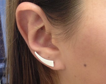 May include: A silver ear cuff with a curved, flat design. The cuff is worn in the upper ear, near the cartilage.