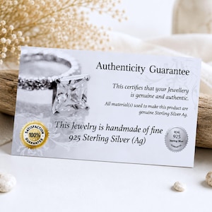 May include: A rectangular white authenticity guarantee card featuring a photograph of a square-cut gemstone ring. The text reads Authenticity Guarantee, This certifies that your Jewellery is genuine and authentic, and This Jewelry is handmade of fine 925 Sterling Silver (Ag).